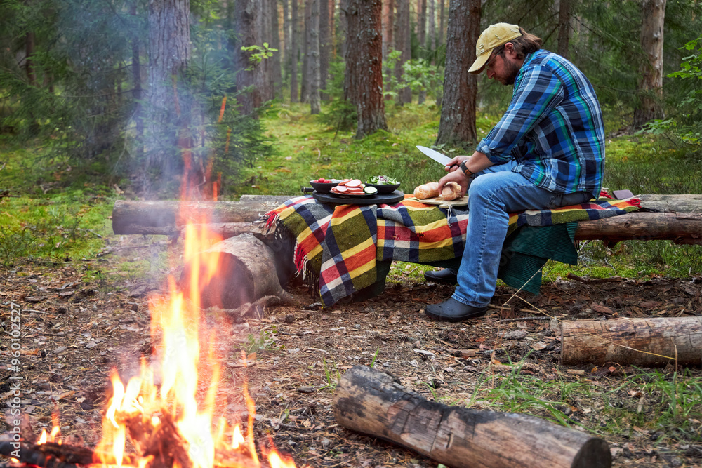 a man sits by a campfire in the woods making sandwiches for a picnic snack a man sits by a campfire in the woods making sandwiches for a picnic snack