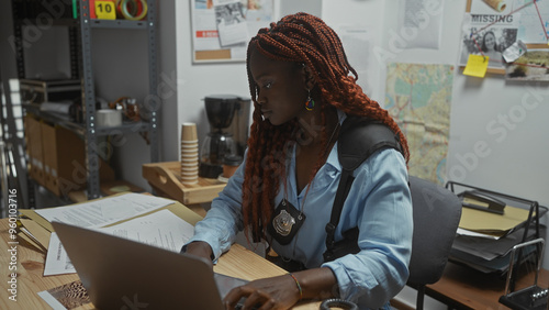 African american woman detective concentrating on work at police station office with laptop and documents. photo