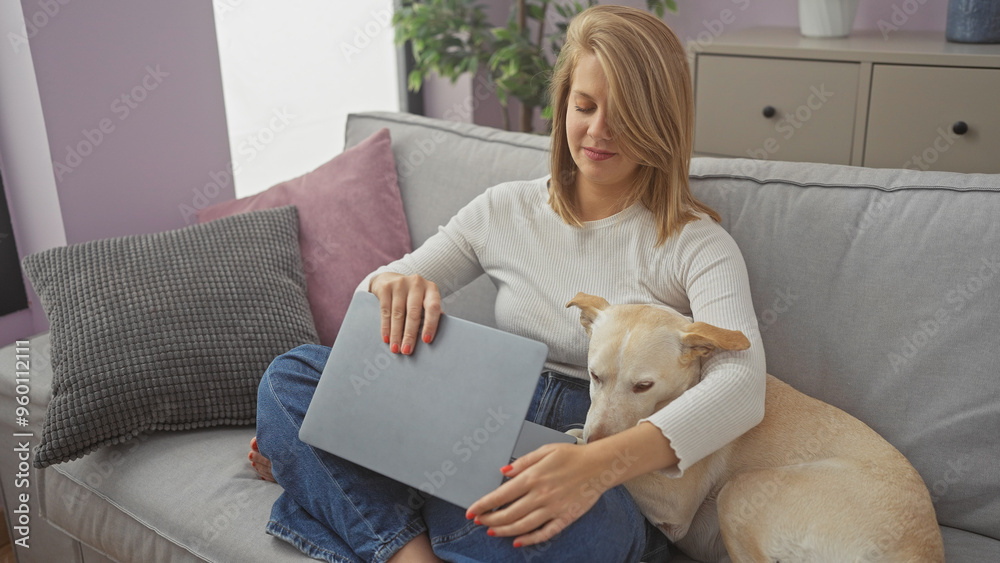 Young adult caucasian woman relaxing with her dog on a couch indoors while using a laptop Young adult caucasian woman relaxing with her dog on a couch indoors while using a laptop