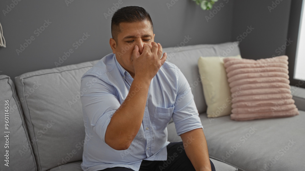 Young man holding his nose while sitting on a couch in a modern living room, implying discomfort or bad smell in a home interior setting. Young man holding his nose while sitting on a couch in a modern living room, implying discomfort or bad smell in a home interior setting.