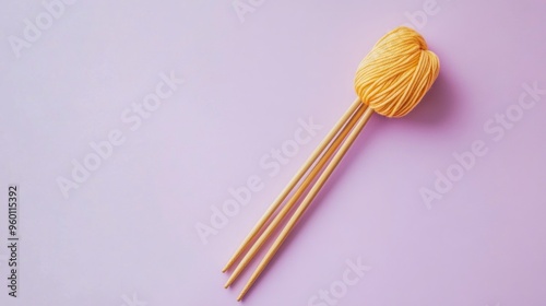 A ball of yellow yarn with knitting needles on a pastel purple background.