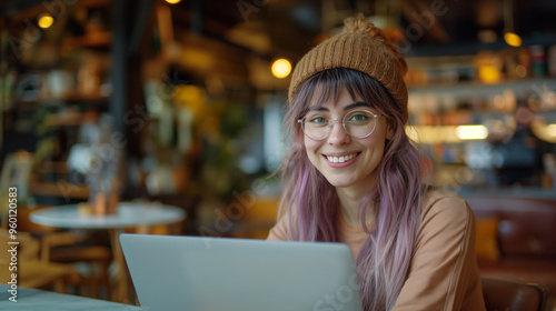 Cheerful young woman with colorful hair working on a laptop in a café.