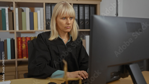 Woman working in office with computer wearing black robe in courtroom with bookshelves in background