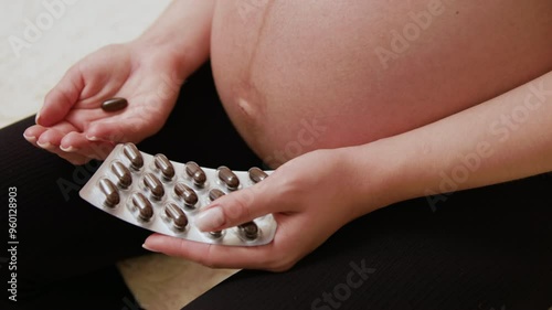 Close-up image of bare belly of a pregnant woman holding special vitamins and supplements for pregnant women. Vitamins and supplements for pregnant women to maintain deficiencies in the body photo