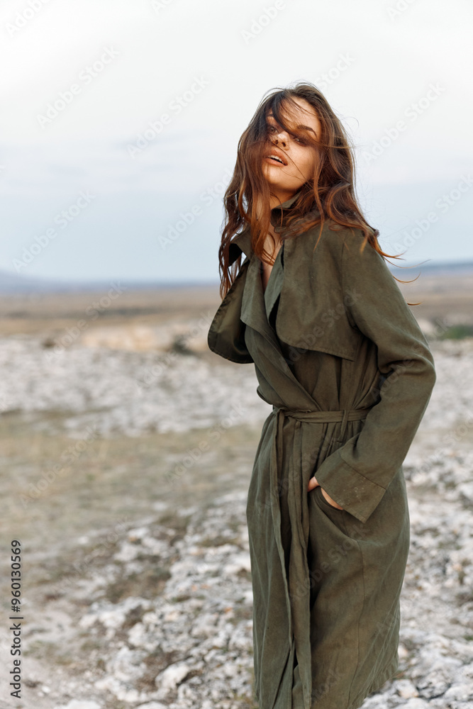 Mysterious woman in trench coat standing on rocky hillside with hands in pockets on overcast day Mysterious woman in trench coat standing on rocky hillside with hands in pockets on overcast day