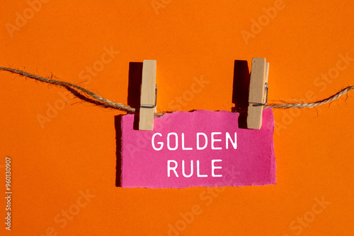 Golden rule message written on ripped torn pink paper piece with orange background. Conceptual golden rule symbol. Copy space.