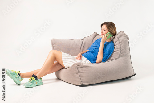 Beautiful girl sitting on poof and talking on phone isolated on white background