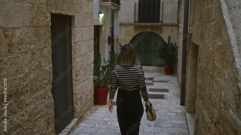 Young hispanic woman walking through narrow stone streets in polignano a mare, puglia, italy, holding a stylish straw bag. Young hispanic woman walking through narrow stone streets in polignano a mare, puglia, italy, holding a stylish straw bag.