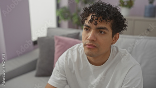 Young hispanic man in thoughtful pose sitting in a modern living room.