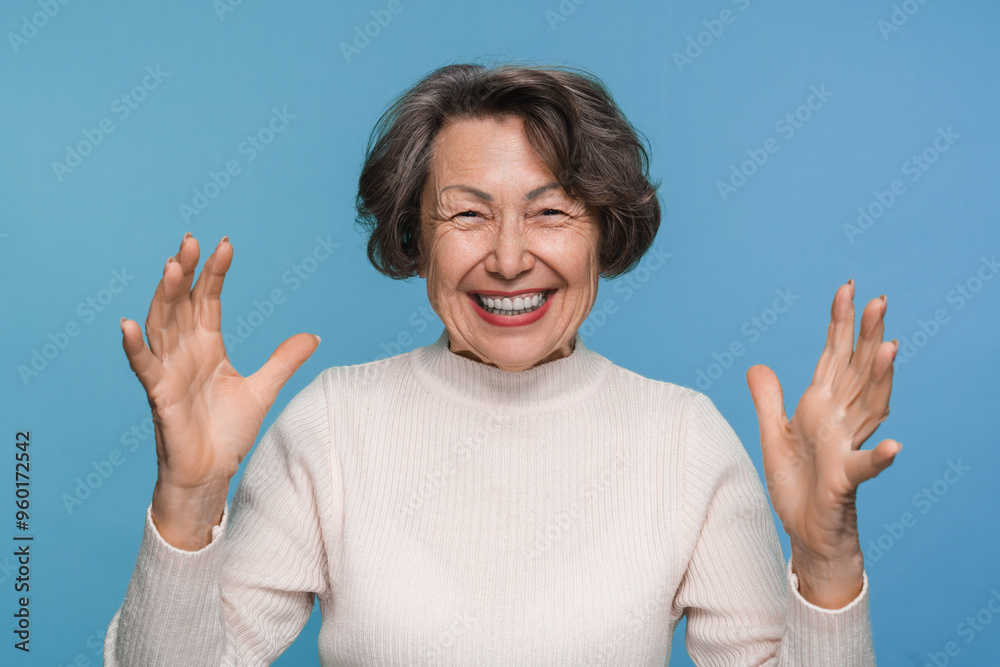 Extremely happy old woman grandmother wearing casual clothes expressing emotions of joy isolated over blue background. Senior elderly granny shouting with excitement Extremely happy old woman grandmother wearing casual clothes expressing emotions of joy isolated over blue background. Senior elderly granny shouting with excitement