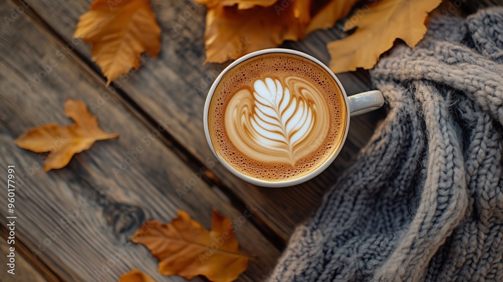 A cup of coffee with latte art with autumn leaves and a knitted sweater on a wooden table, top view. A cup of coffee with latte art with autumn leaves and a knitted sweater on a wooden table, top view.