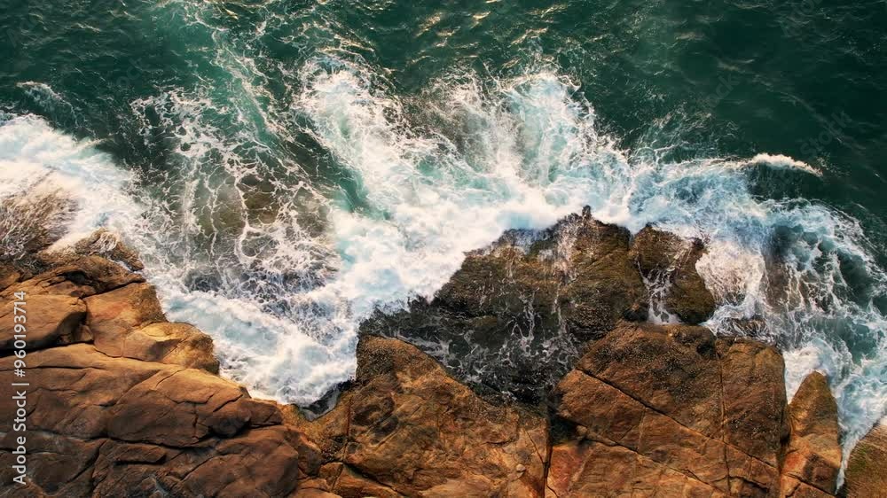 Aerial view over the waves crashing against the rocks. Turquoise Ocean Waves Crash Against Rocky Coastline, moody sea weaving around boulder-strewn coastlines Aerial view over the waves crashing against the rocks. Turquoise Ocean Waves Crash Against Rocky Coastline, moody sea weaving around boulder-strewn coastlines