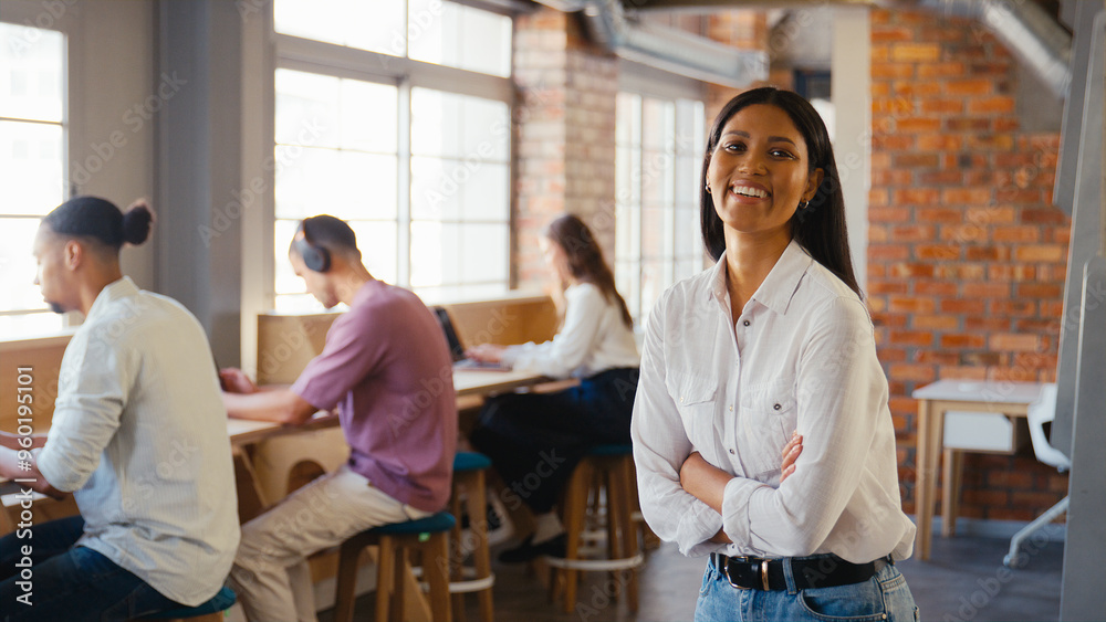 Portrait Of Young Smiling Businesswoman Working In Open Plan Office With Colleagues In Background Portrait Of Young Smiling Businesswoman Working In Open Plan Office With Colleagues In Background
