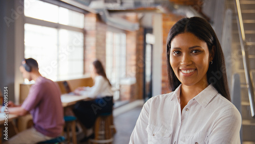 Portrait Of Young Smiling Businesswoman Working In Open Plan Office With Colleagues In Background