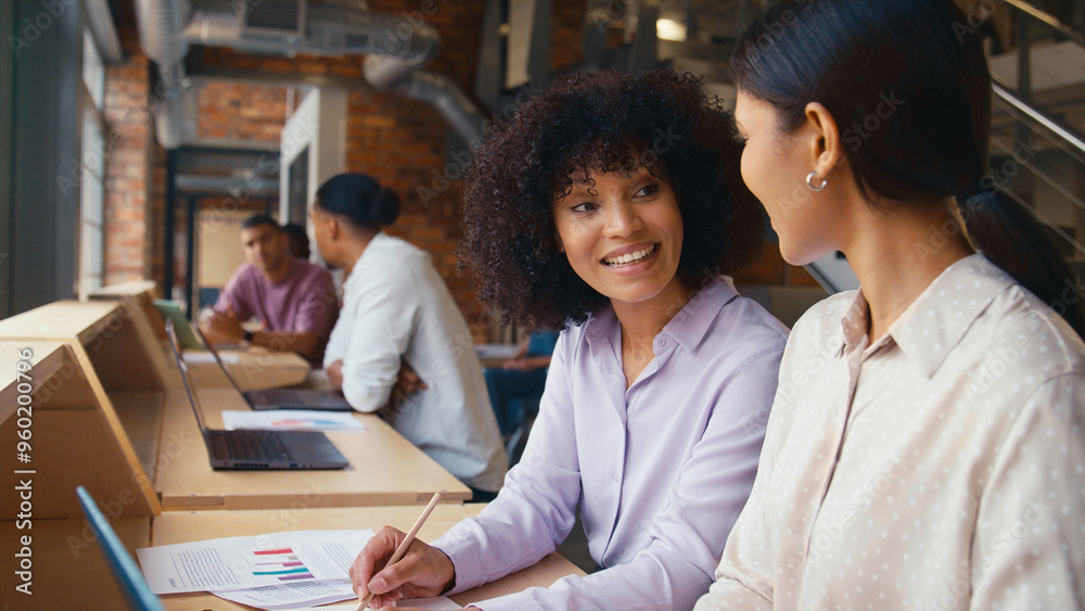 Two Businesswomen With Laptop Meeting In Office Discussing Documents With Colleagues In Background Two Businesswomen With Laptop Meeting In Office Discussing Documents With Colleagues In Background