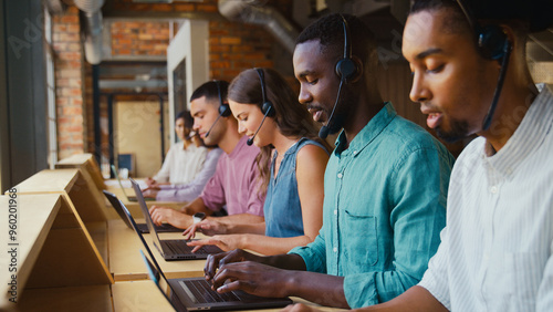 Multi-Cultural Customer Support Or Telesales Team In Modern Open Plan Office Wearing Headsets