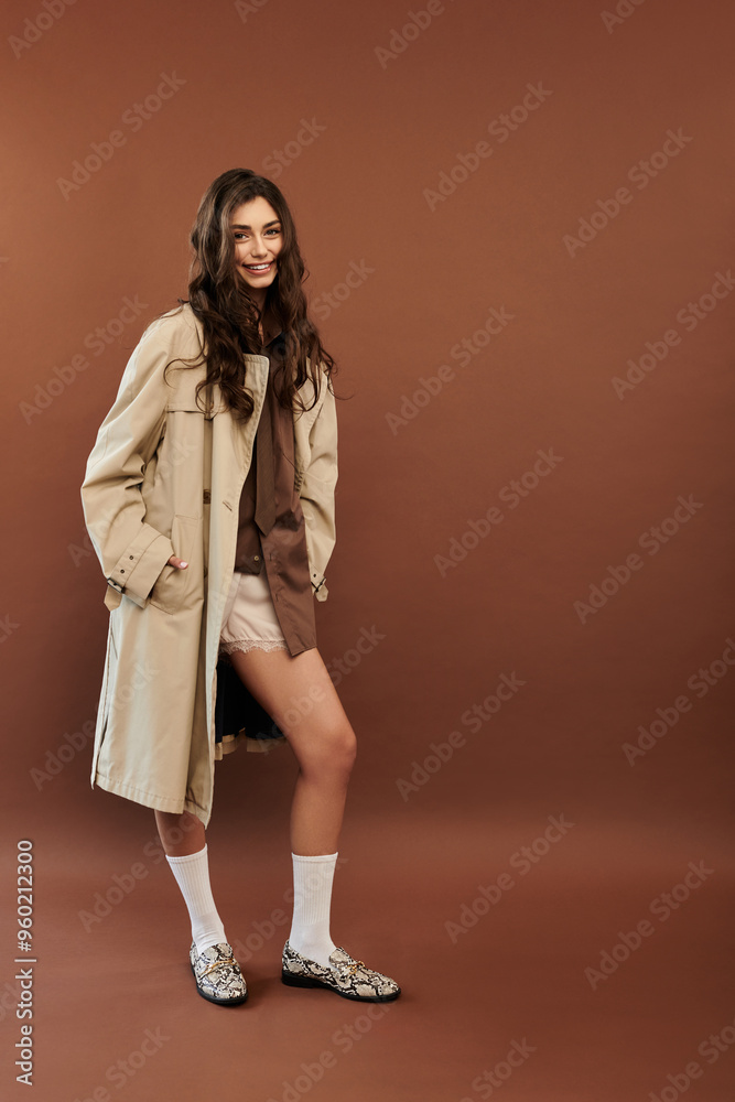 A young woman exudes confidence in a stylish autumnal outfit, posing effortlessly against a warm brown backdrop. A young woman exudes confidence in a stylish autumnal outfit, posing effortlessly against a warm brown backdrop.