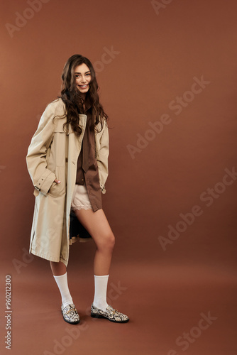 A young woman exudes confidence in a stylish autumnal outfit, posing effortlessly against a warm brown backdrop.