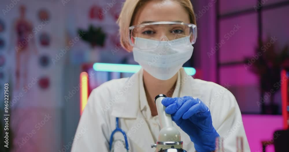 Doctor woman chemist in protective mask,eyewear and gloves learning samples under microscope in evening lab Doctor woman chemist in protective mask,eyewear and gloves learning samples under microscope in evening lab