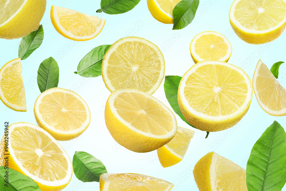 Fresh juicy lemons and green leaves falling on light blue background