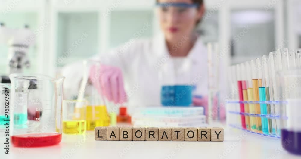 Tiny wooden cubes arranged on table to form word LABORATORY. Young woman scientist in lab coat prepares samples for experiment slow motion Tiny wooden cubes arranged on table to form word LABORATORY. Young woman scientist in lab coat prepares samples for experiment slow motion