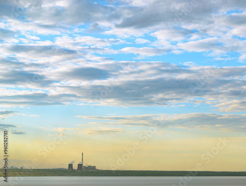 CHP and other plants stand on the shore of the lake in the evening under clouds in the sky