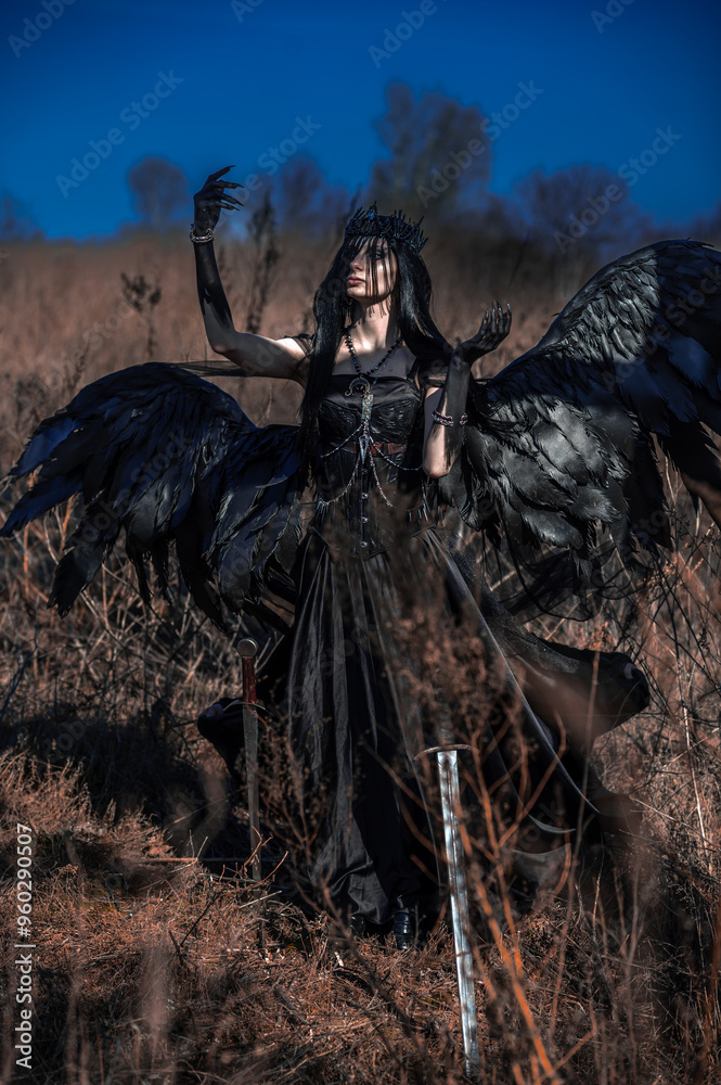 Fototapeta premium Goddess of death with black wings on a dried field