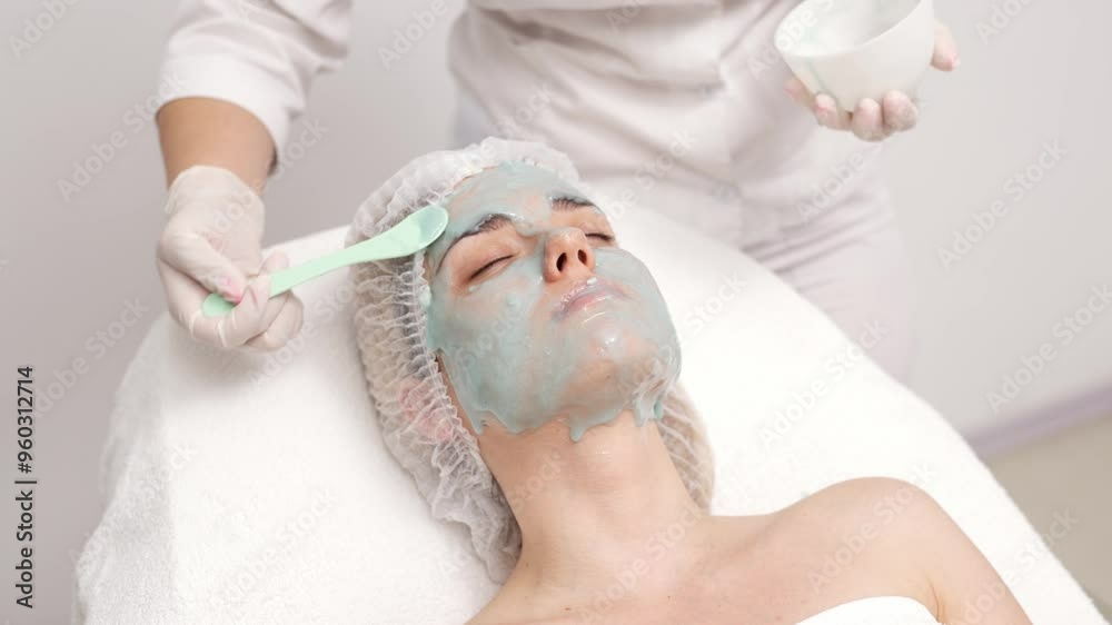 A young woman receives a revitalizing alginate face mask from a skilled cosmetologist in a sleek, modern beauty clinic. Perfect for promoting premium skincare treatments in your ads.