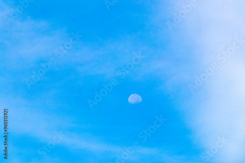 Crescent half full moon in blue sky during the day.