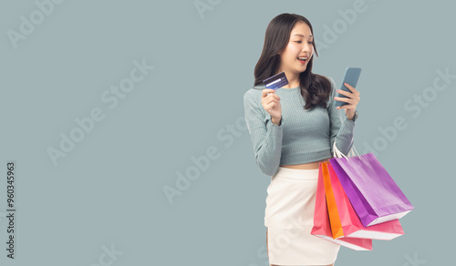 Young asian lady using mobile phone holding credit card carry shopping bags isolated over pastel green background and copy space Smiling young girl purchasing online through phone using credit card