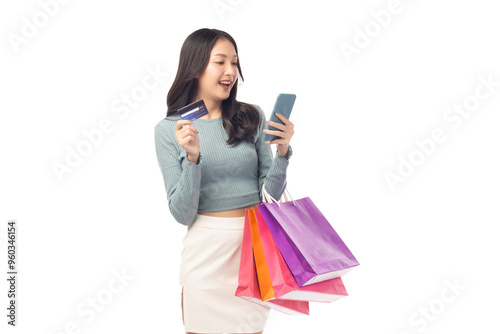 Young asian lady using mobile phone holding credit card carry shopping bags isolated over pastel green background and copy space Smiling young girl purchasing online through phone using credit card