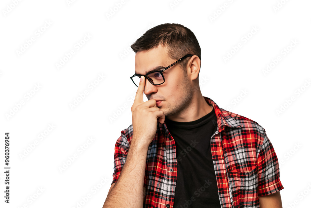 Young man deep in thought wearing glasses and a plaid shirt. A young man with glasses in a plaid shirt touches his face, appearing lost in thought against a plain background. Young man deep in thought wearing glasses and a plaid shirt. A young man with glasses in a plaid shirt touches his face, appearing lost in thought against a plain background.