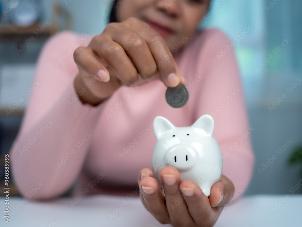 Woman wearing a pink shirt put coins in the piggy bank for saving money and financial concept, Business banking and financial concept, Saving money for retirement funds and insurance concept. Woman wearing a pink shirt put coins in the piggy bank for saving money and financial concept, Business banking and financial concept, Saving money for retirement funds and insurance concept.