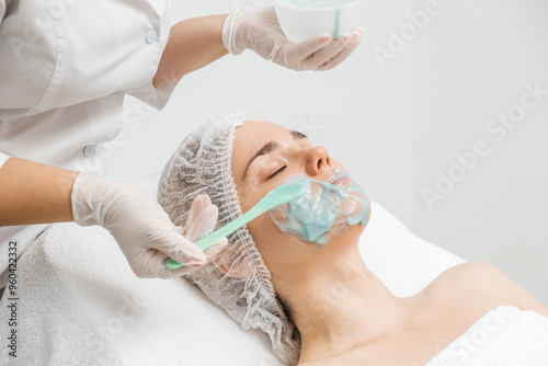 A young woman receives a revitalizing alginate face mask from a skilled cosmetologist in a sleek, modern beauty clinic. Perfect for promoting premium skincare treatments in your ads. photo