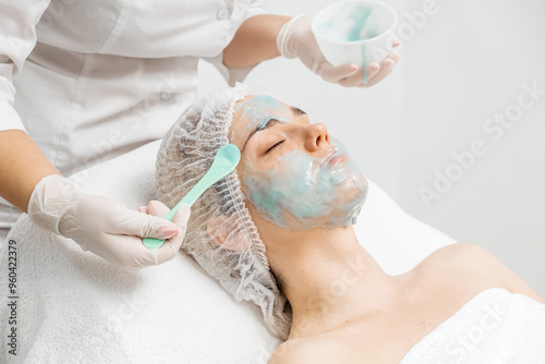 A young woman receives a revitalizing alginate face mask from a skilled cosmetologist in a sleek, modern beauty clinic. Perfect for promoting premium skincare treatments in your ads. photo