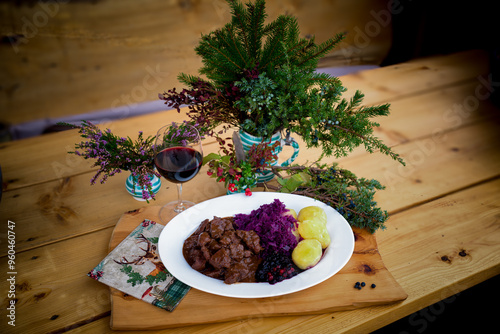 ready to eat and served on a white plate on a wood table - goulash from venison meat with potatoes, red cabbage and craneberries -  cooked on a charcoal grill at outdoor photo