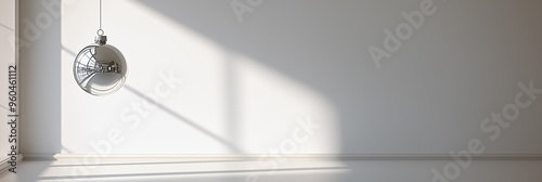 A single reflective silver Christmas ornament hangs in a bright, minimalist space. The natural light and shadows create a serene, modern holiday composition.