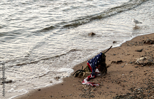 Bandera de los Estados Unidos a orillas del río Este en Nueva York, Estados Unidos. Vieja bandera maltrecha arrastrada por el río hasta la orilla arenosa de la isla de Manhattan.