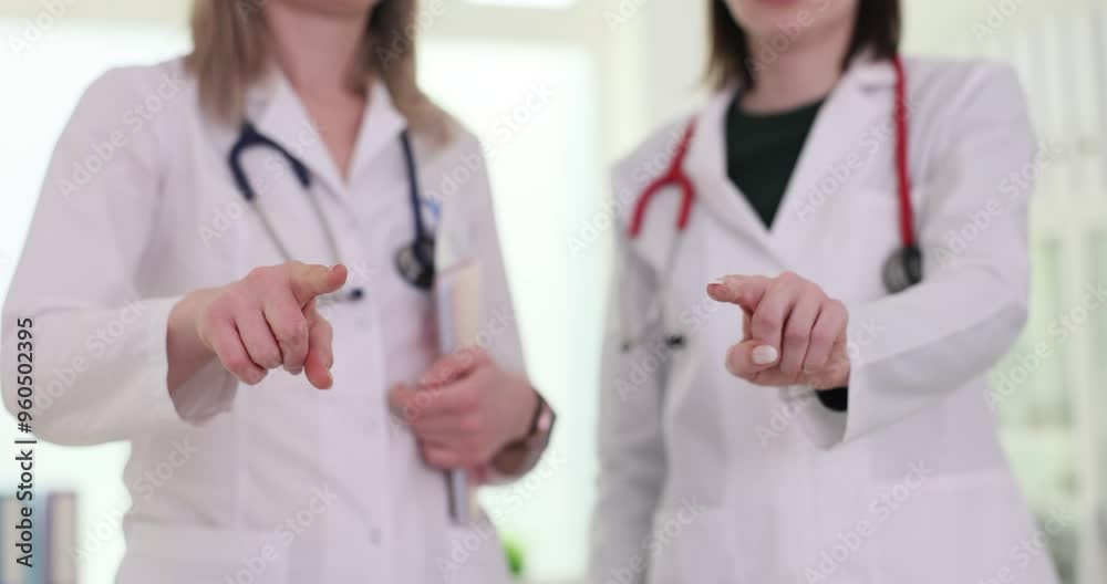 Female doctors in white coats point index fingers forward. Women signal readiness to address next challenge or direct attention to important matter Female doctors in white coats point index fingers forward. Women signal readiness to address next challenge or direct attention to important matter