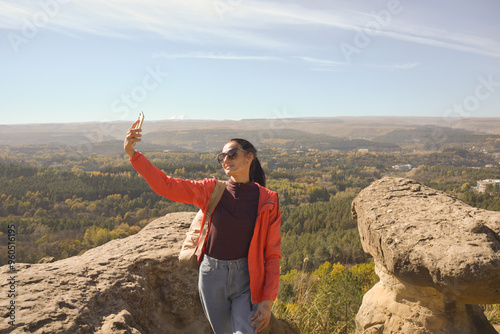 Young beautiful woman traveler taking selfie portrait on mountain top - Happy smiling girl using smartphone - Hiking and climbing rock