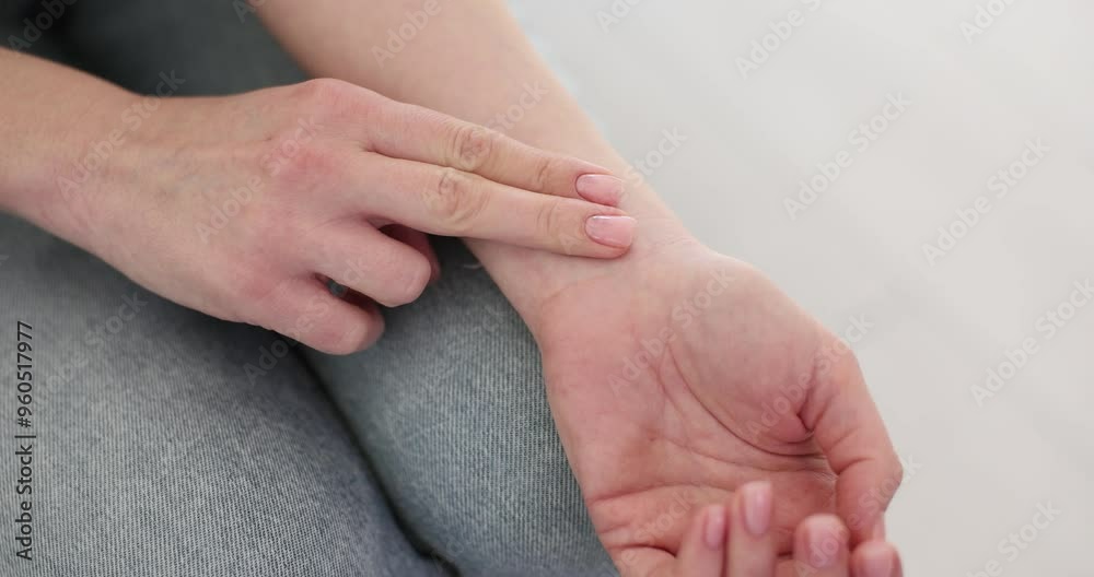 Female puts fingers on wrist measuring pulse sitting on sofa. Exhausted woman checks heartbeat feeling fatigue after hard working day Female puts fingers on wrist measuring pulse sitting on sofa. Exhausted woman checks heartbeat feeling fatigue after hard working day