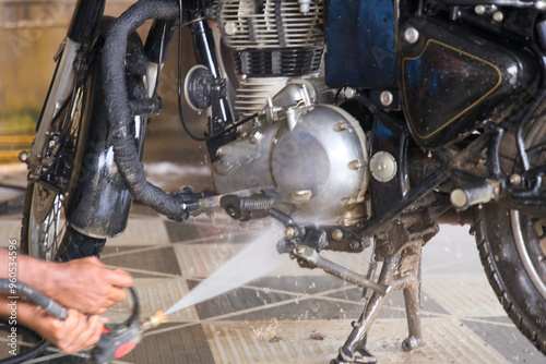 A person washing a motorcycle engine with a pressure washer at a bike cleaning station in the morning