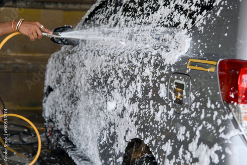 Person washing a car with foam and water at a car wash station during daylight hours photo