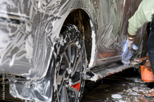 Car being washed with soap and foam at a service station during the daytime with a person cleaning the vehicles exterior