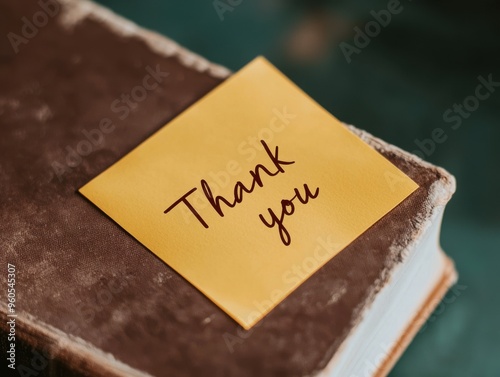 A yellow sticky note with Thank you written in neat handwriting, attached to the cover of a closed book