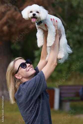 Portrait of smiling young woman kiss dog in Natural Park. Dog lover woman wearing blue dress with dog during good day. Concept of friendship and beautiful girl with a small dog