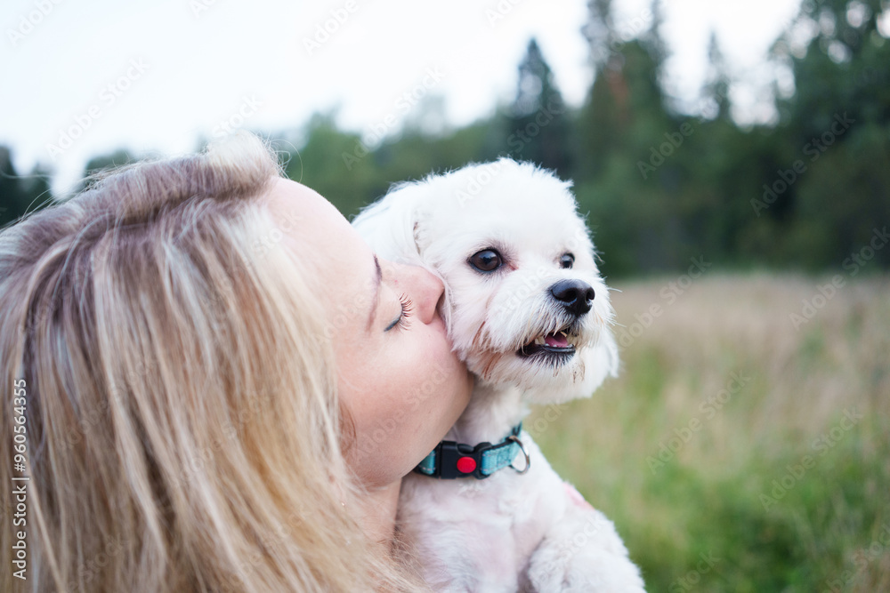 Portrait of smiling young woman kiss dog in Natural Park. Dog lover woman wearing blue dress with dog during good day. Concept of friendship and beautiful girl with a small dog Portrait of smiling young woman kiss dog in Natural Park. Dog lover woman wearing blue dress with dog during good day. Concept of friendship and beautiful girl with a small dog