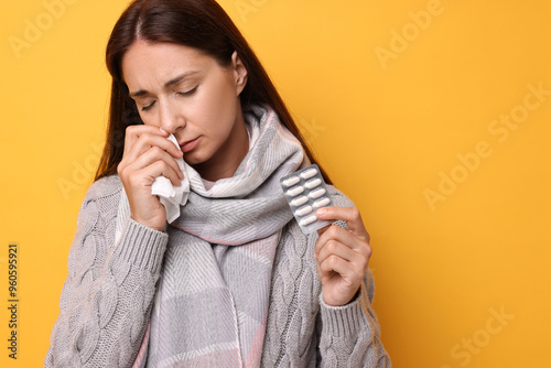 Sick woman with tissue and pills on orange background. Cold symptoms