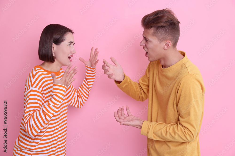 Emotional young couple arguing on pink background Emotional young couple arguing on pink background