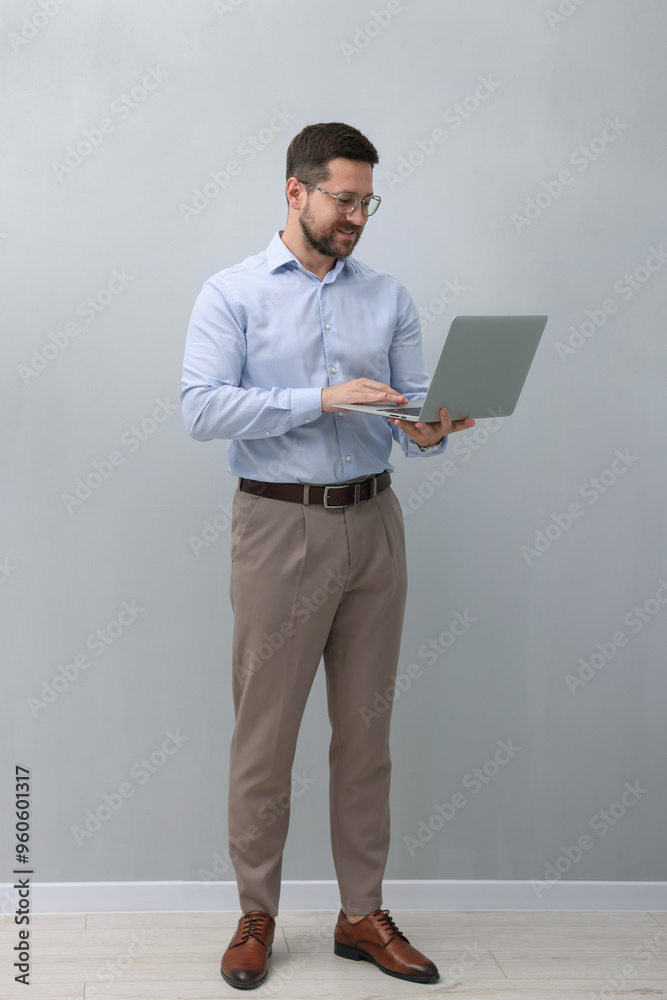 Businessman using laptop near grey wall indoors Businessman using laptop near grey wall indoors